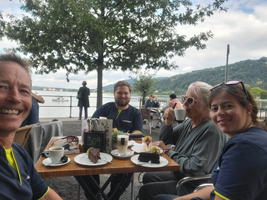 Vier Personen am Tisch, genießen Kaffee und Kuchen mit Blick auf den See.