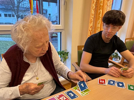 Eine ältere Frau und ein junger Mann spielen zusammen Karten.