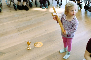Ein Mädchen hält ein Holzkreuz neben einem goldenen Kelch und einer Platten.
