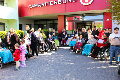 Eine Gruppe älterer Menschen, begleitet von Kindern, vor einem Gebäude des Samariterbundes.