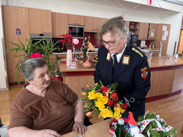 Eine Frau in Uniform überreicht einer älteren Dame einen Blumenstrauß.