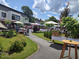 Markt mit Ständen, Besuchern und vielen Pflanzen an einem sonnigen Tag.