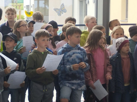 Eine Gruppe von Kindern singt und hält Blätter in den Händen.