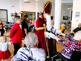 Eine Gruppe von Menschen feiert mit St. Nikolaus in einem Gemeinschaftsraum.