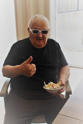 Älterer Mann mit Sonnenbrille, gibt Daumen hoch und hält einen Dessertteller.