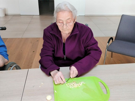 Eine ältere Frau schneidet Gemüse auf einem grünen Schneidebrett.