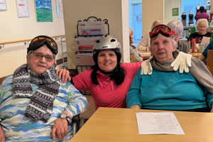 Drei Frauen in Skiausrüstung lächeln gemeinsam in einem gemütlichen Raum.