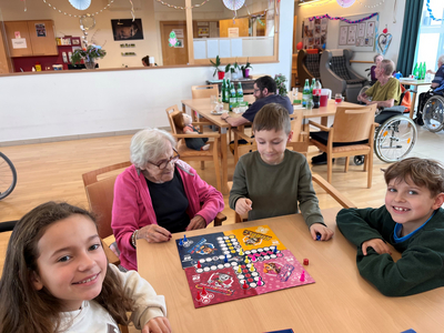 Vier Kinder und eine ältere Frau spielen gemeinsam Gesellschaftsspiele an einem Tisch.