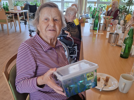 Eine Seniorin hält eine transparente Box mit buntem Inhalt in der Hand.