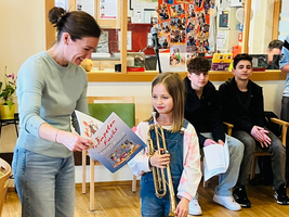 Ein Mädchen mit Trompete steht neben einer Frau und hält ein Buch.