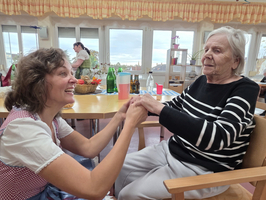 Eine Frau hält die Hände einer älteren Dame und lächelt sie an.