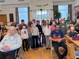 Kinder mit Füchsenmasken stehen in einer Gemeinschaftsräume voller Senioren.
