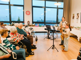Zwei Kinder spielen Musik vor einer Gruppe von älteren Menschen in einem Raum.