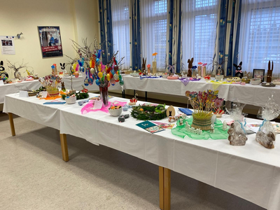 Bunte Osterdekorationen und Kunsthandwerk auf mehreren Tischen in einem Raum.