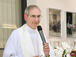 Ein Priester spricht mit einem Mikrofon vor einer Blumendekoration.