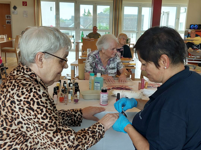 Seniorinnen genießen eine Nagelpflege in einem Gemeinschaftsraum.