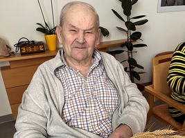 Ein älterer Mann sitzt und arbeitet mit Weizenhalmen.