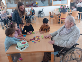 Kinder spielen mit einem älteren Mann am Tisch in einem Gemeinschaftsraum.