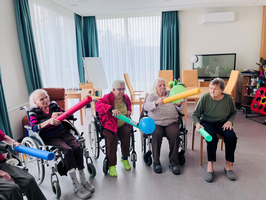 Ältere Frauen in Rollstühlen halten bunte Röhren und spielen gemeinsam in einem Raum.