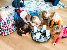 Kinder liegen um einen Adventskranz mit Kerzen und bewundern ihn.