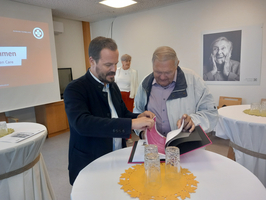 Zwei Männer betrachten gemeinsam ein Buch in einem hellen Raum.