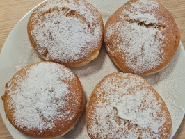 Vier mit Puderzucker bestreute, runde Gebäckstücke auf einem weißen Teller.