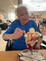 Eine ältere Person genießt ein Eisbecher mit Sahne und Erdbeersoße.