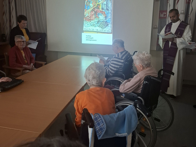 Eine Gruppe älterer Menschen sitzt in einem Raum und verfolgt eine Präsentation.