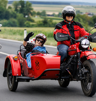 Eine Frau mit Sonnenbrille winkt aus einem roten Motorradgespann.