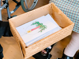 Eine Hand hält eine Box mit kunstvoller Zeichnung und Papierblättern.