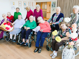 Eine Gruppe älterer Frauen sitzt in Rollstühlen, umgeben von Blumen.