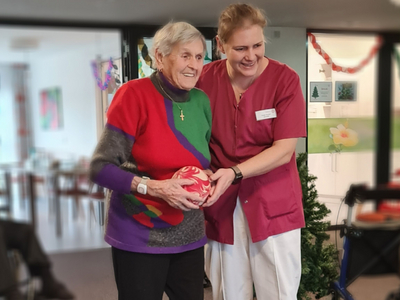 Eine ältere Frau und eine Mitarbeiterin halten gemeinsam einen ballförmigen Gegenstand.
