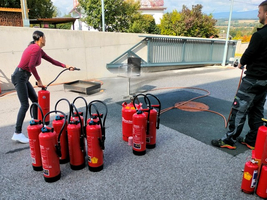 Eine Person übt den Einsatz eines Feuerlöschers mit mehreren Löschgeräten in der Nähe.