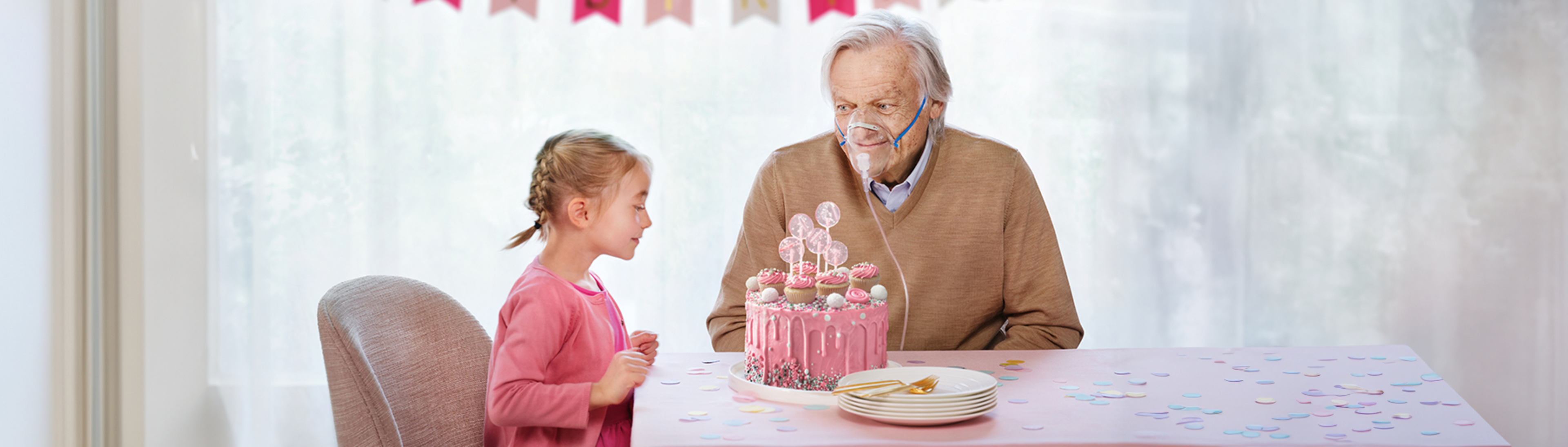 Geburtstagskind sitzt mit seinem Opa bei Tisch mit Geburtstagstorte
