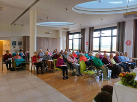 Eine Gruppe älterer Menschen sitzt in einem Raum und hört aufmerksam zu.