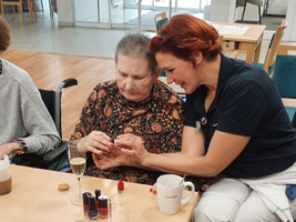 Eine Frau zeigt einer älteren Dame das Auftragen von Nagellack.