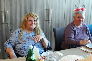 Zwei ältere Frauen sitzen an einem Tisch und lächeln freundlich.