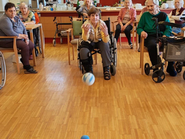 Senioren spielen Bowling mit blauen Kegeln in einem Gemeinschaftsraum.