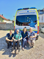 Vier Personen lächeln vor einem Krankenwagen mit der Aufschrift 