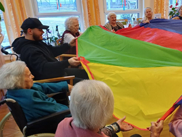 Ältere Menschen und Betreuer spielen mit einem bunten Spieltuch.