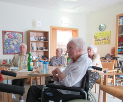 Ältere Menschen sitzen zusammen bei einer Veranstaltung, Essen und Getränke auf dem Tisch.