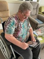 Eine ältere Frau im Rollstuhl schaut aufmerksam auf ein Tablet.
