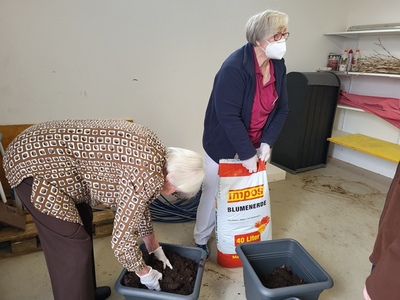 Zwei Frauen füllen Blumenerde in Behälter.