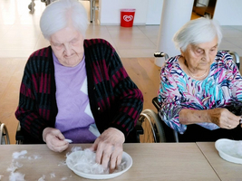 Zwei ältere Frauen in Rollstühlen sortieren Daunen auf einem Tisch.