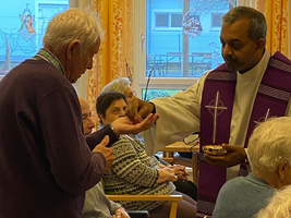 Ein Priester reicht einem älteren Mann eine Segnung im Pflegeheim.
