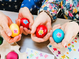 Hände halten bunte, verzierte Ostereier mit Schmetterlingsmotiven.