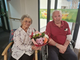 Ein älteres Paar sitzt zusammen, die Frau hält einen Blumenstrauß in den Händen.