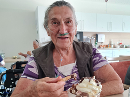 Ältere Frau isst ein Eis in einem gemütlichen Raum.