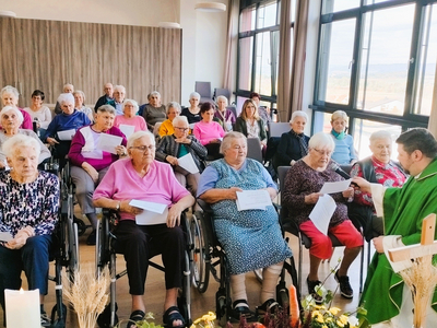 Eine Versammlung älterer Menschen bei einer religiösen Zeremonie in einem hellen Raum.