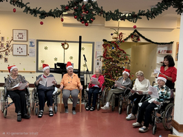 Senioren in Rollstühlen singen Weihnachtslieder vor einem geschmückten Baum.